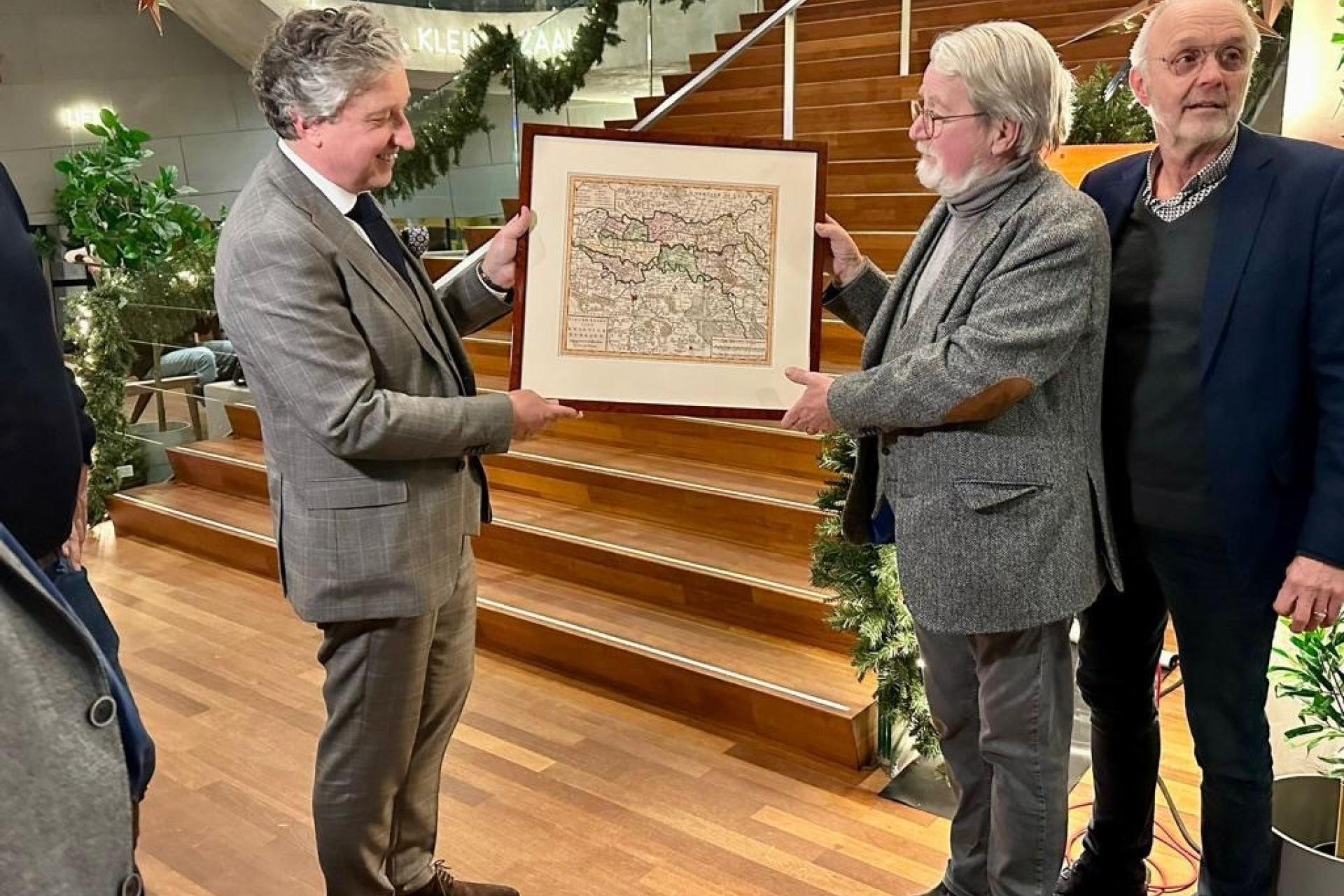 Drie mannen, links burgemeester krijgt een oude kaart van het Rivierengebied ingelijst aangeboden. 